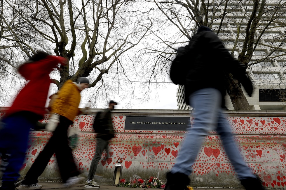 Quattro passanti, in primo piano, camminano lungo il muro 