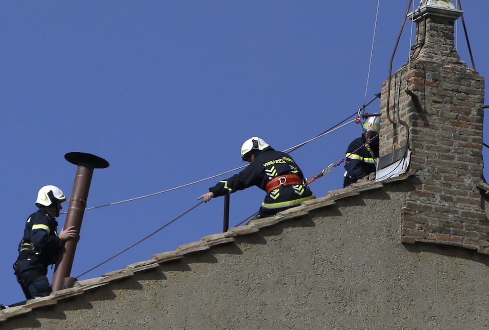 Tre vigili del fuoco trasportano il comignolo in cima al tetto