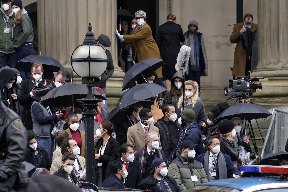 Un gruppo di persone indossa una mascherina all'aperto, in piedi sulle scalinate dell'edificio