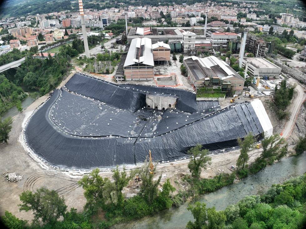 Fotografia dall'alto di un'area industriale cittadina in cui un vasto terreno è coperto da teloni neri
