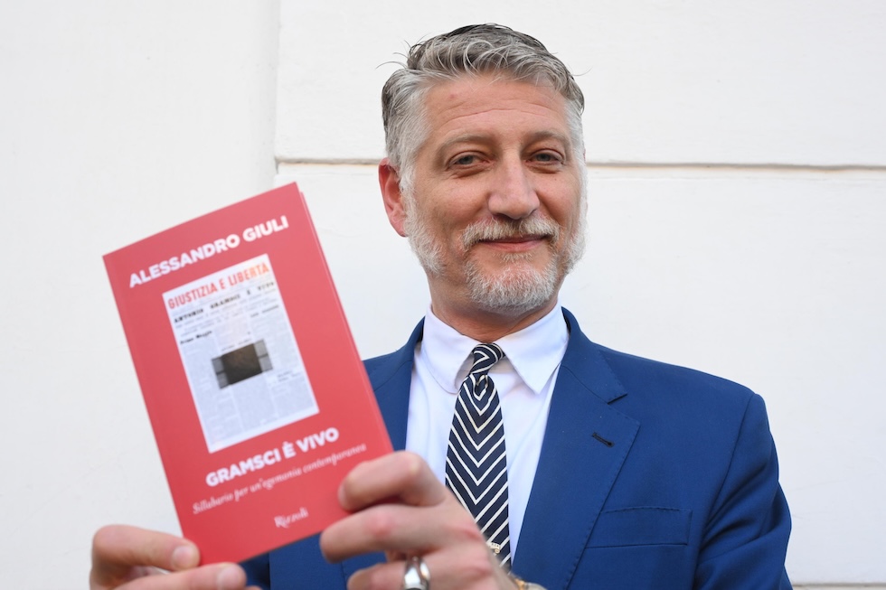 Il ministro Giuli sorride verso l'obiettivo mentre regge una copia del suo libro