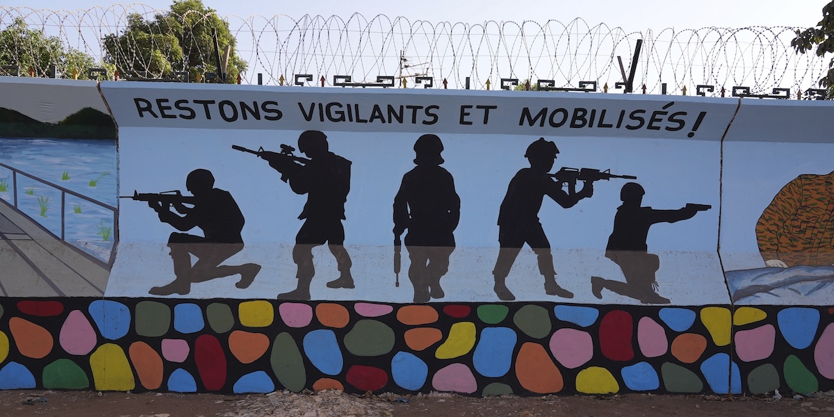 Un murale a Ouagadougou che rappresenta dei soldati; sopra il muro c'è del filo spinato