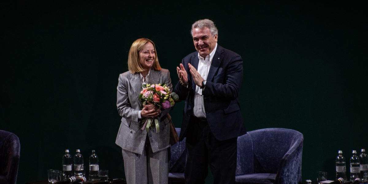 giorgia meloni, con un mazzo di fiori, e luigi sbarra sopra a un palco