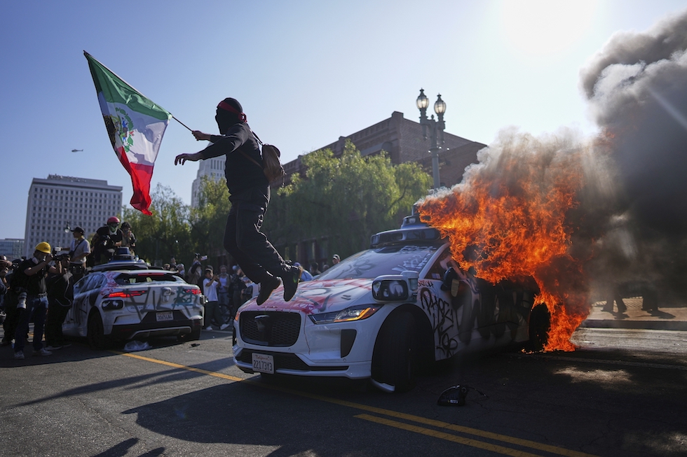 Un manifestante sopra un'auto di Waymo in fiamme, 8 giugno 2025