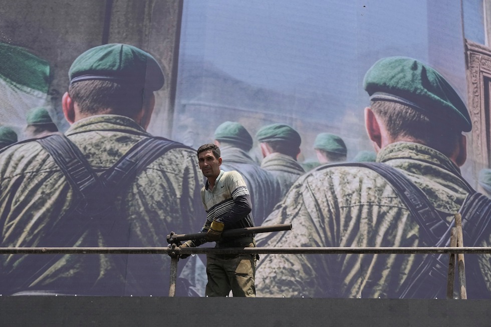 Un operaio davanti a un manifesto anti israeliano a Teheran, 14 giugno 2025