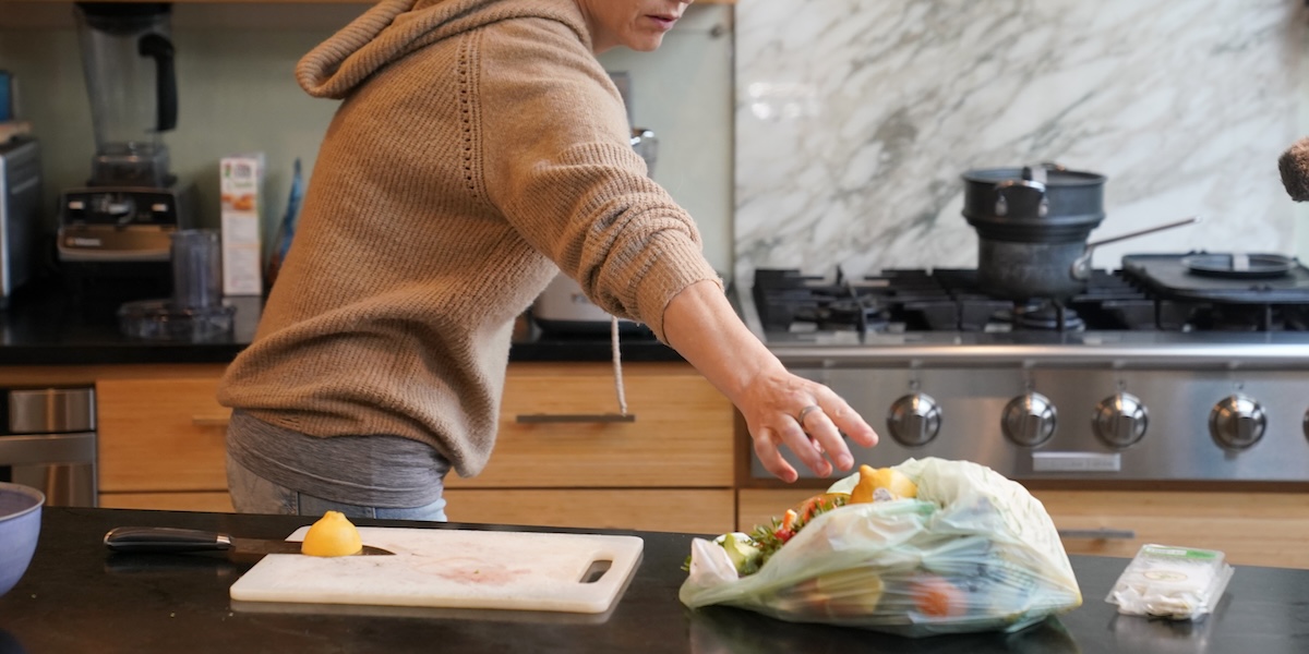 Una donna getta una buccia di limone in un sacchetto per la spazzatura compostabile
