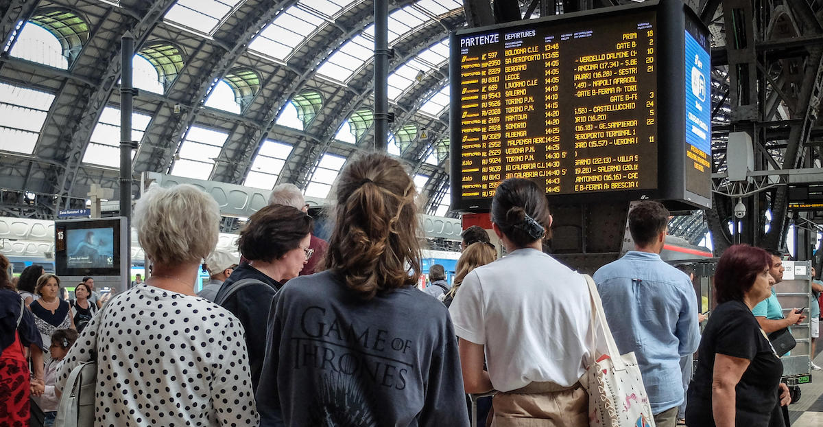 Persone davanti l tabellone della stazione Centrale di Milano