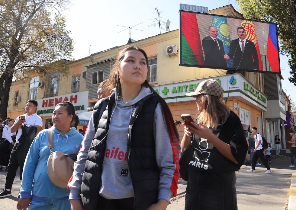 Alcune donne camminano davanti a uno schermo che mostra una foto di Japarov insieme al presidente russo Vladimir Putin, a Bishkek, la capitale del Kirghizistan, nel 2023