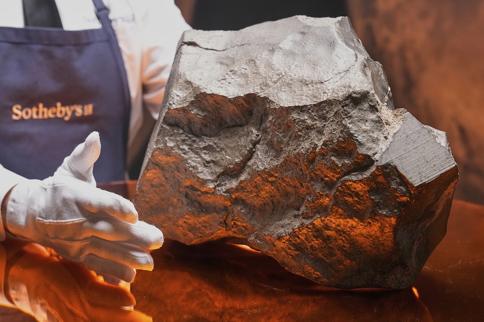 Il meteorite maneggiato da una curatrice di Sotheby’s che indossa dei guanti bianchi 
