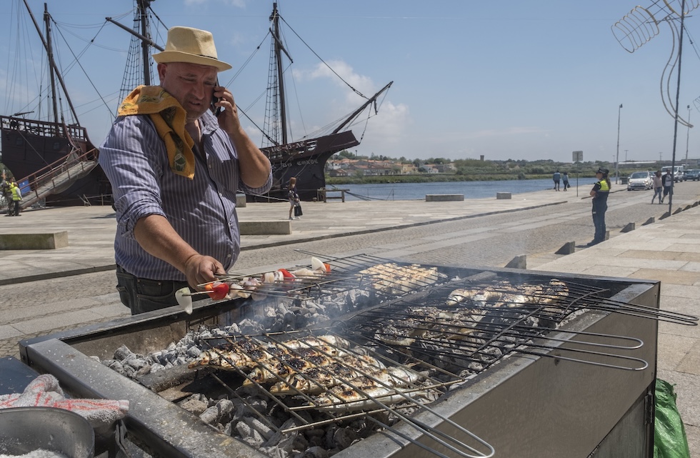 Un uomo parla al telefono mentre rigira il cibo sulla griglia