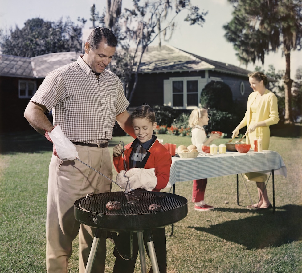 Padre e figlio si occupano del barbecue, mentre madre e figlia apparecchiano la tavola alle loro spalle