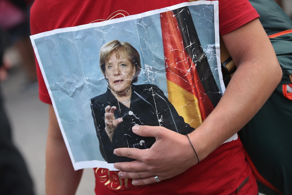 Una persona migrante con una fotografia di Angela Merkel al suo arrivo in Germania, nel 2015