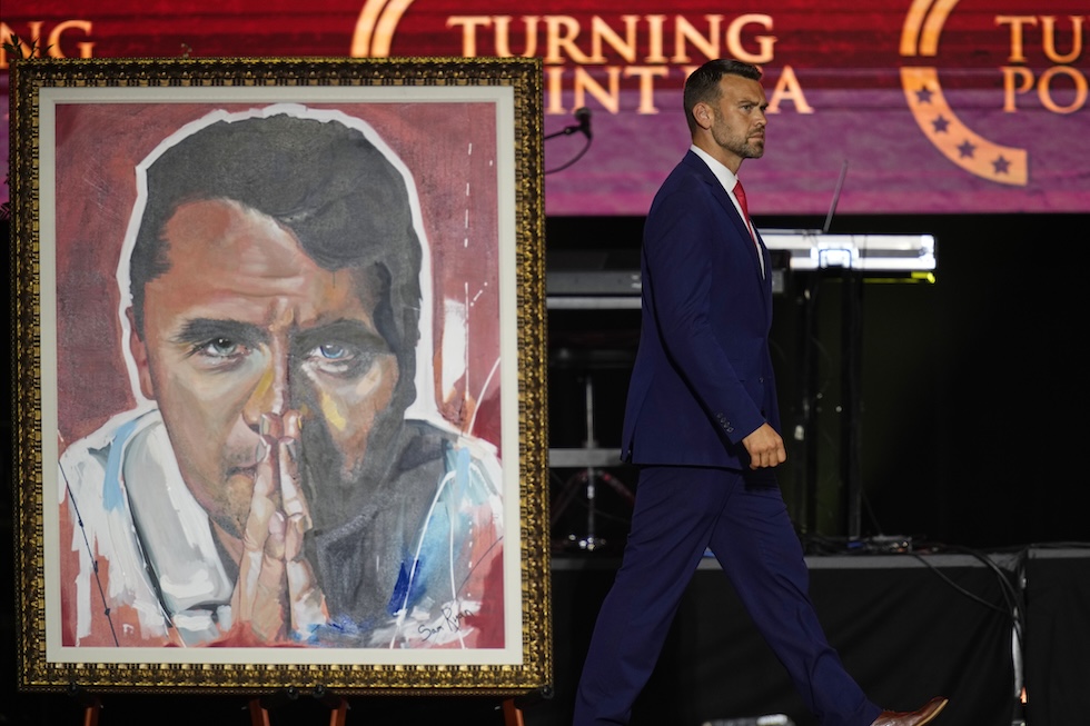 Il ritratto di Kirk in preghiera sul palco, dove sta salendo l'attivista Jack Posobiec 