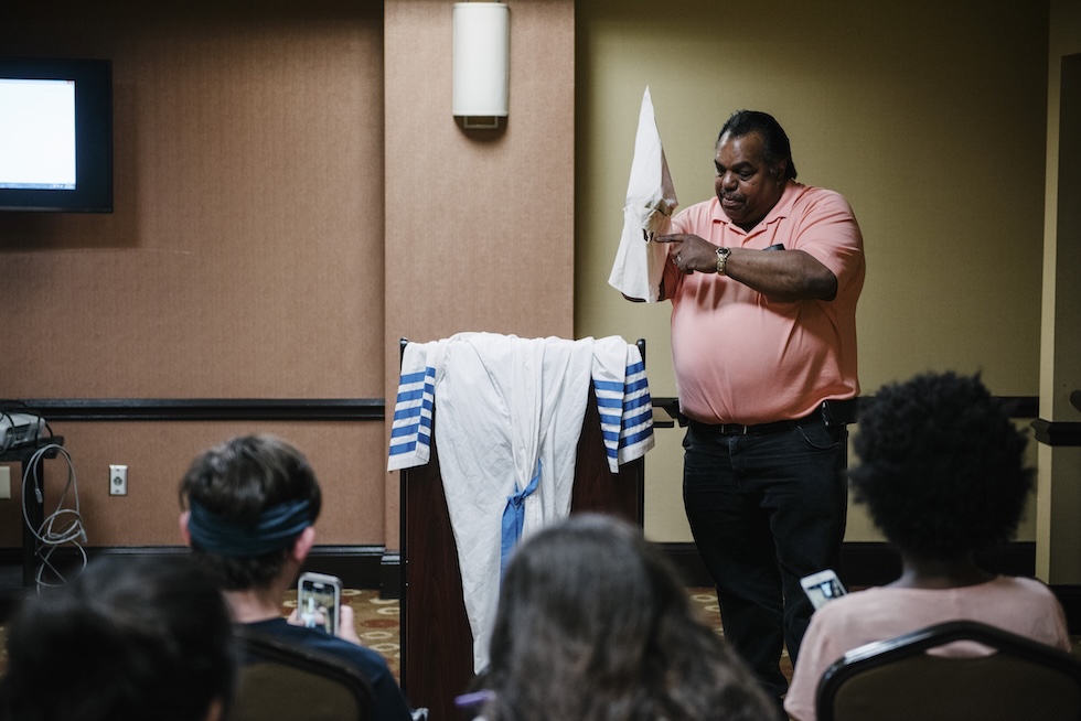 Daryl Davis regge in mano un cappuccio davanti a un gruppo di persone sedute ad ascoltarlo