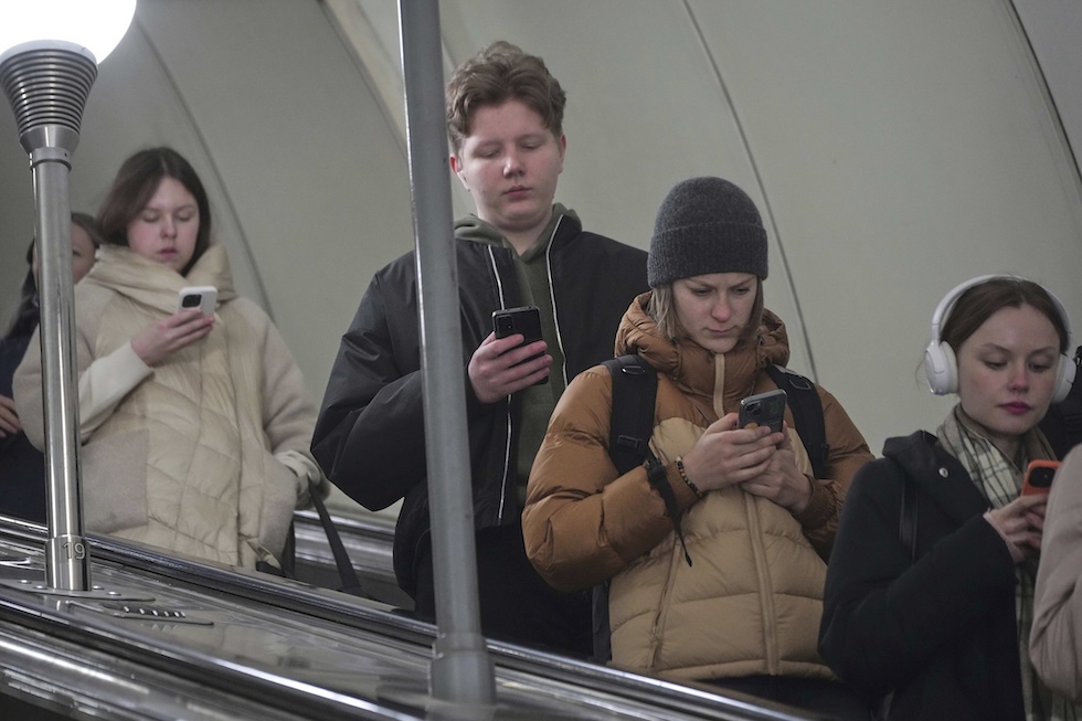 Un gruppo di giovani mentre scende le scale mobili con lo sguardo fisso sugli smartphone