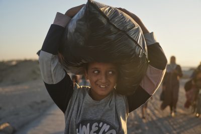 Un ragazzino trasporta una borsa sulla testa, mentre si dirige lungo il litorale verso la città di Gaza