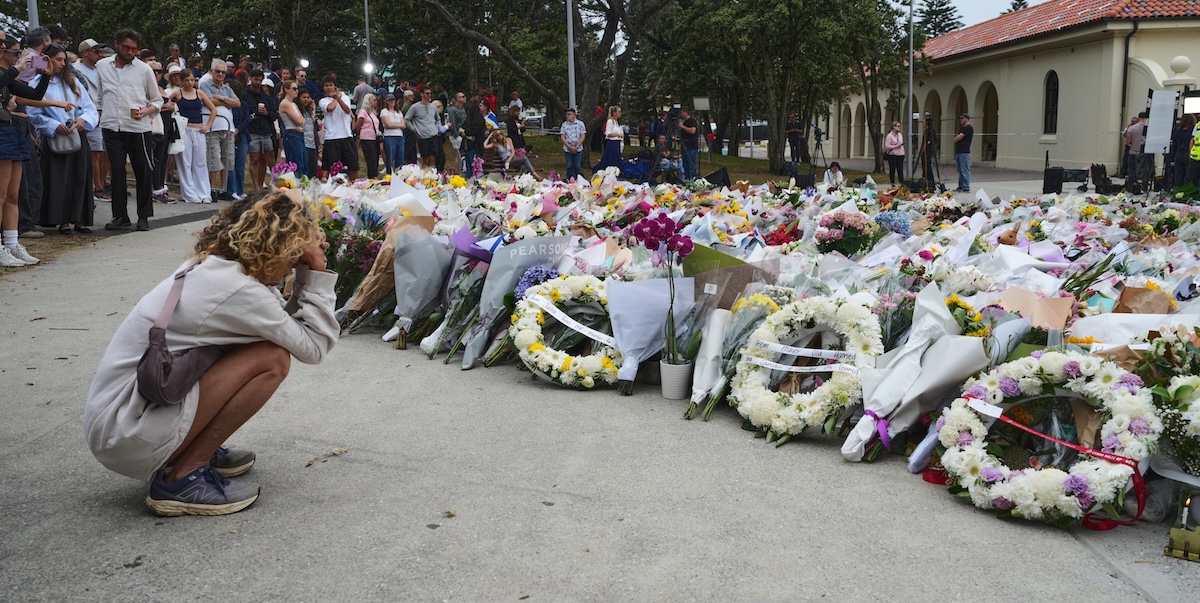 Una donna si inginocchia davanti a dei fiori a Bondi Beach, Sydney, Australia, 16 dicembre 2025 (AP Photo/Mark Baker)