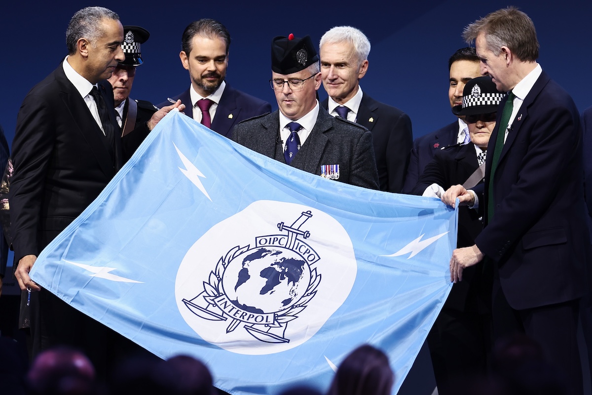 Mohamed Dkhissi, il direttore della Polizia Giudiziaria del Marocco (al centro), con la bandiera dell'Interpol a una sessione della propria assemblea generale il 7 novembre 2024 a Glasgow, in Scozia (Getty Images/Jeff J Mitchell)
