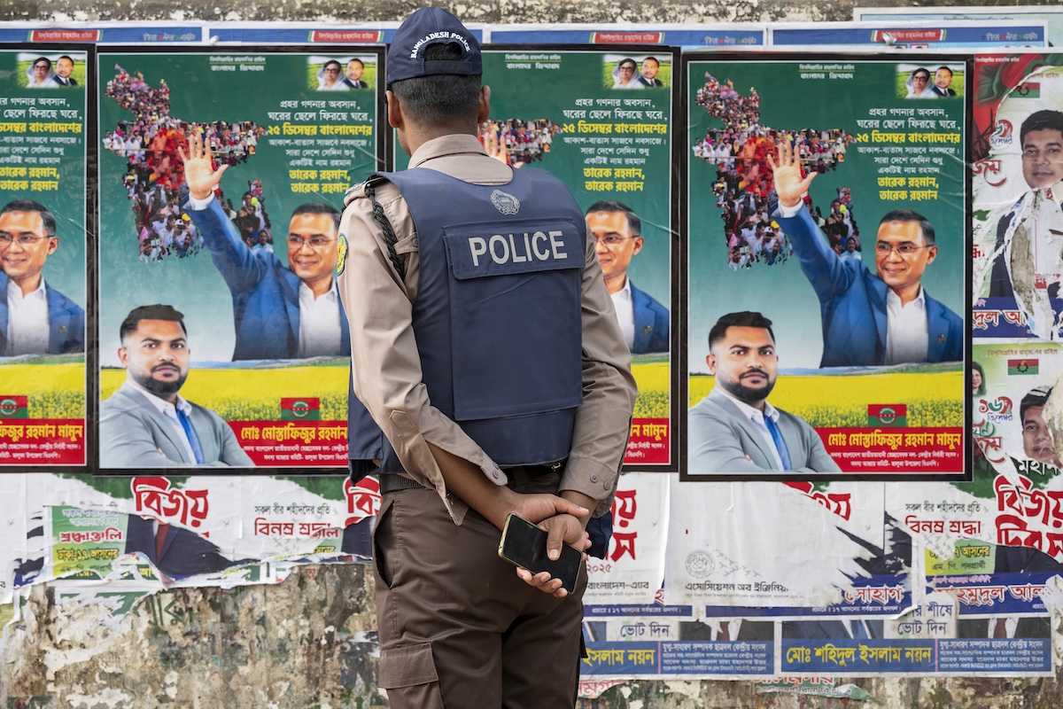 Un poliziotto davanti ad alcuni manifesti del Partito Nazionalista, il 21 gennaio a Dacca 