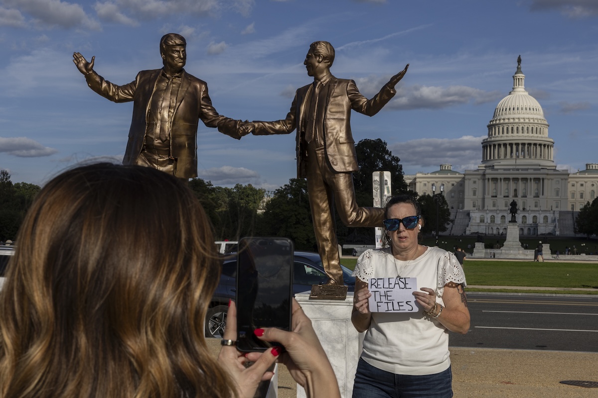 Una manifestante regge un cartello con scritto “release the files" vicino alla scultura