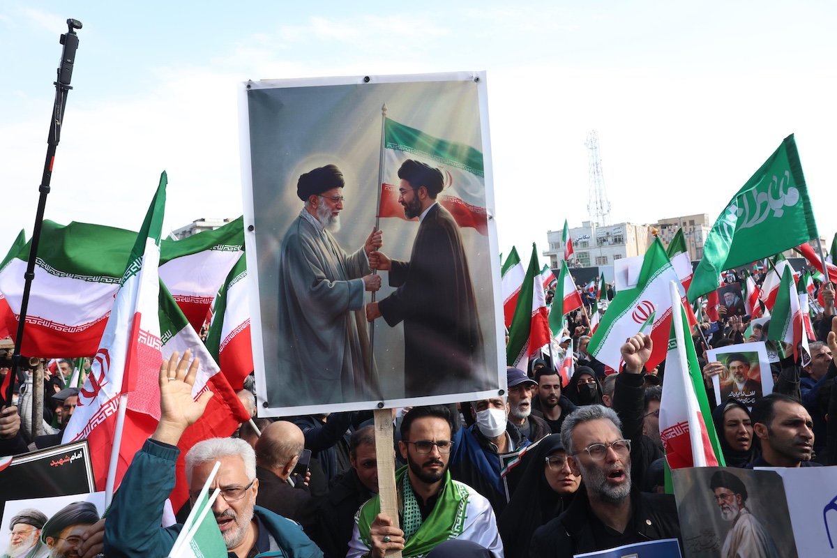 Una persona con un cartello che mostra Ali Khamenei passare una bandiera iraniana al figlio, il 9 marzo a Teheran