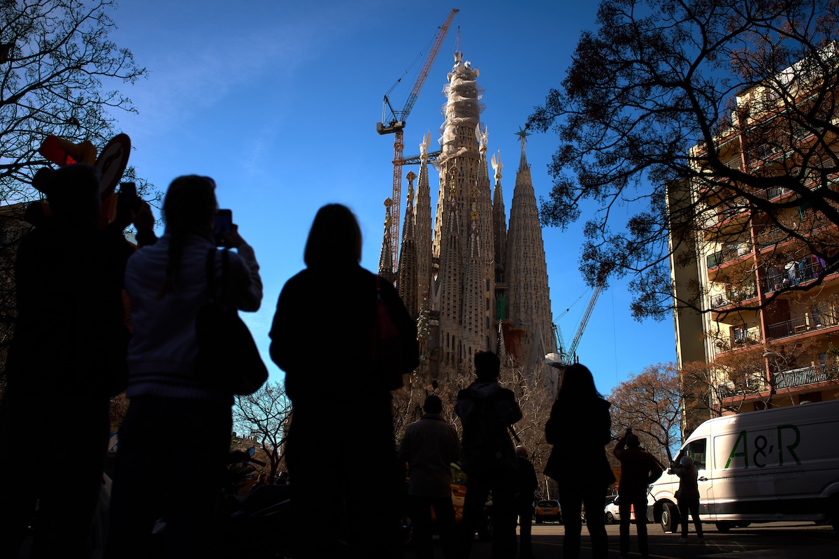 Passanti filmano la posa dell'ultimo pezzo della croce sulla torre di Gesù, 20 febbraio 2026, Barcellona (AP Photo/Emilio Morenatti)