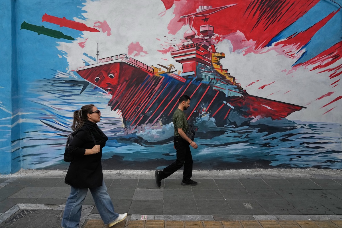 Alcuni passanti davanti a un murale di propaganda del regime iraniano a Teheran (AP Photo/Vahid Salemi)