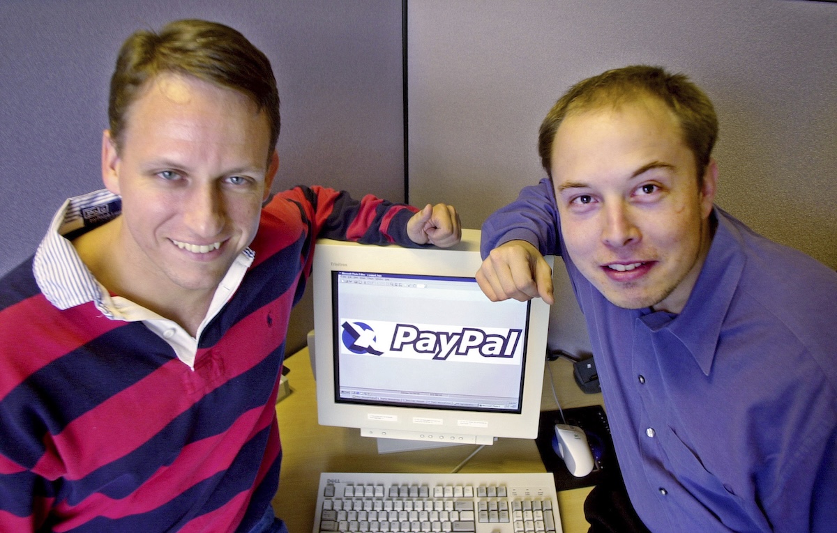 Peter Thiel e Elon Musk, entrambi con un braccio appoggiato su un pc sul cui schermo compare il logo di PayPal