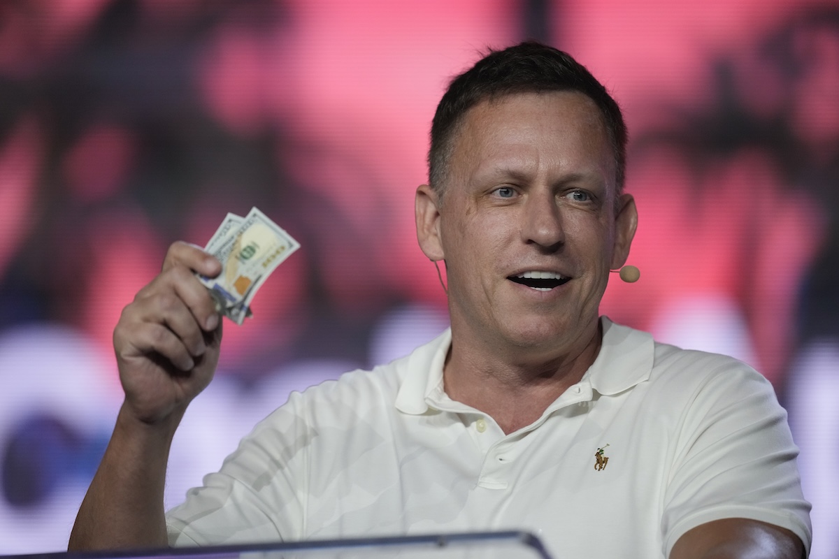 Peter Thiel mentre regge una banconota parlando da un palco