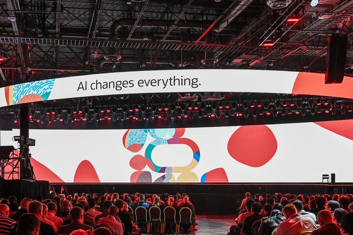 Il pubblico di un evento seduto in un enorme salone, con la scritta "AI changes everything" su un grande schermo