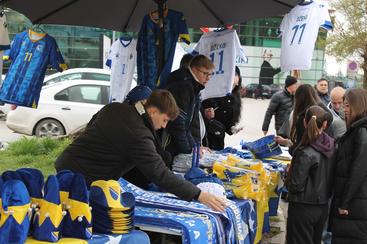Alcuni venditori a una bancarella di magliette e souvenir della nazionale della Bosnia Erzegovina a Zenica, il 31 marzo 2026 (Il Post)