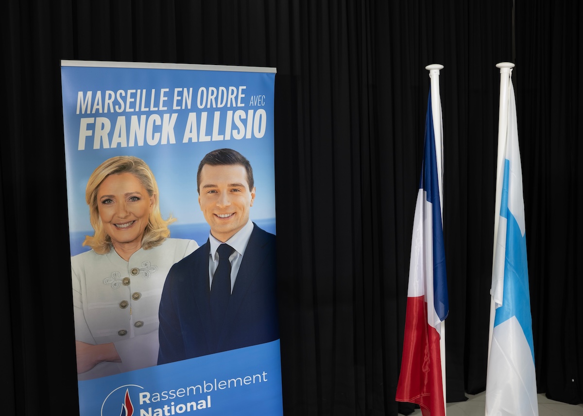 Un poster coi ritratti di Le Pen e Bardella, la bandiera francese e quella di Marsiglia ma non quella europea sul palco di un comizio del candidato dell'estreame destra a Marsiglia, Franck Allisio, il 22 marzo