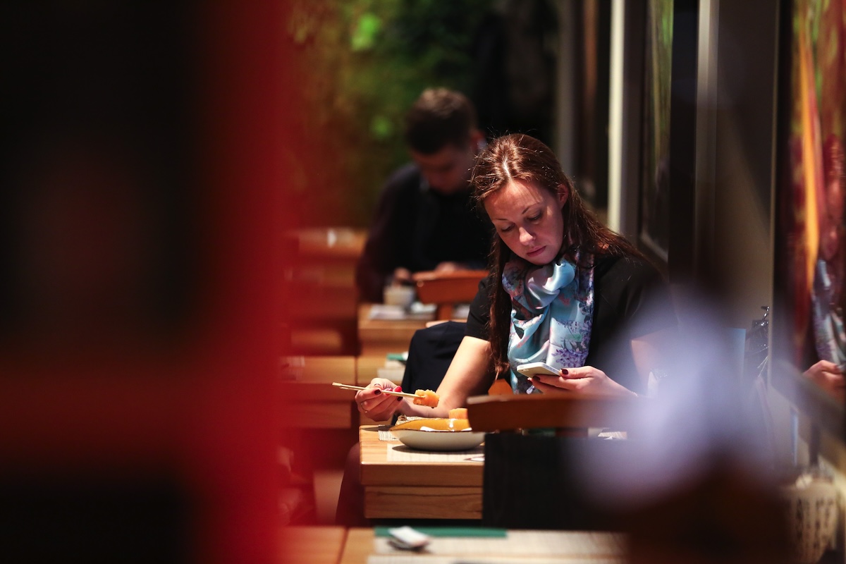 Due clienti seduti in due tavolini distanti guardano ciascuno il loro smartphone