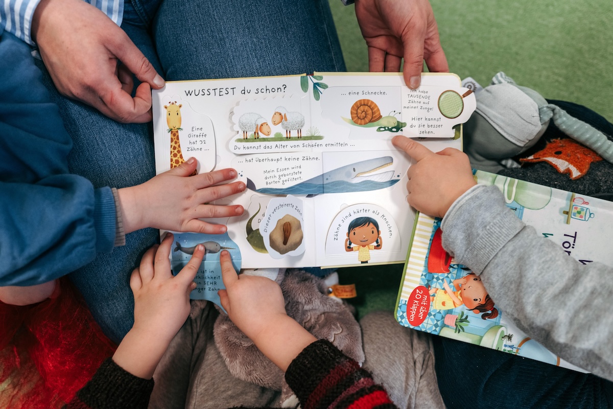 Le mani dei bambini sulle pagine di un libro aperto, sorretto da una maestra