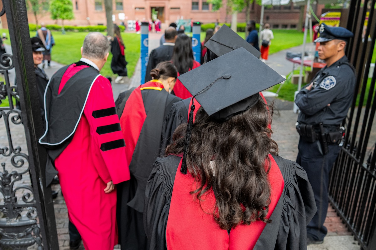 Una laureanda di spalle, in primo piano, al cancello di ingresso dell'università