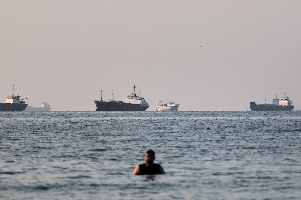 Una persona fa il bagno con le navi mercantili dello stretto di Hormuz a fare da sfondo (Amirhosein Khorgooi/ISNA via AP)