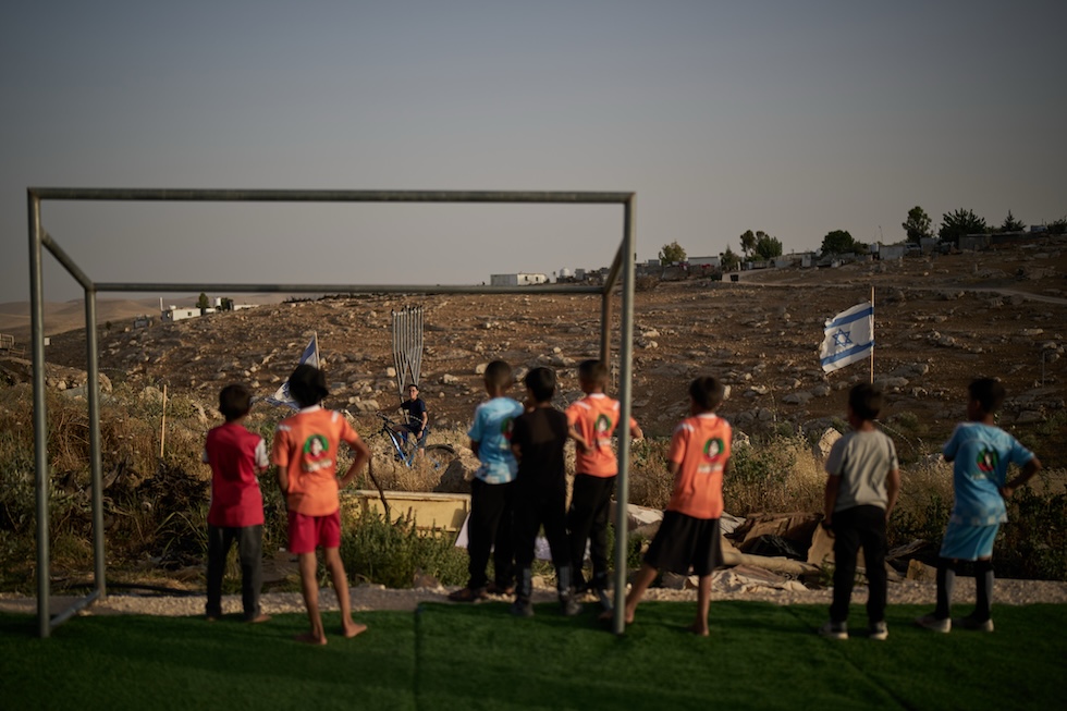 Bambini palestinesi guardano un giovane colono israeliano dopo che il loro pallone da calcio è finito oltre la recinzione di filo spinato che circonda il campo dove stavano giocando, vicino all'insediamento israeliano di Carmel, ed è stato portato via. La foto è stata scattata il 12 maggio e fa parte di un reportage sul calcio in Cisgiordania, dove da più di due anni il campionato palestinese è sospeso (AP Photo/Leo Correa)
