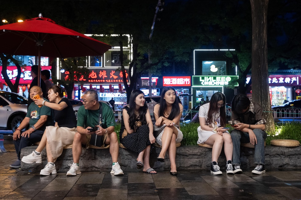 Persone sedute in un'aiuola che aspettano di entrare in un ristorante (ANSA/EPA/JESSICA LEE)
