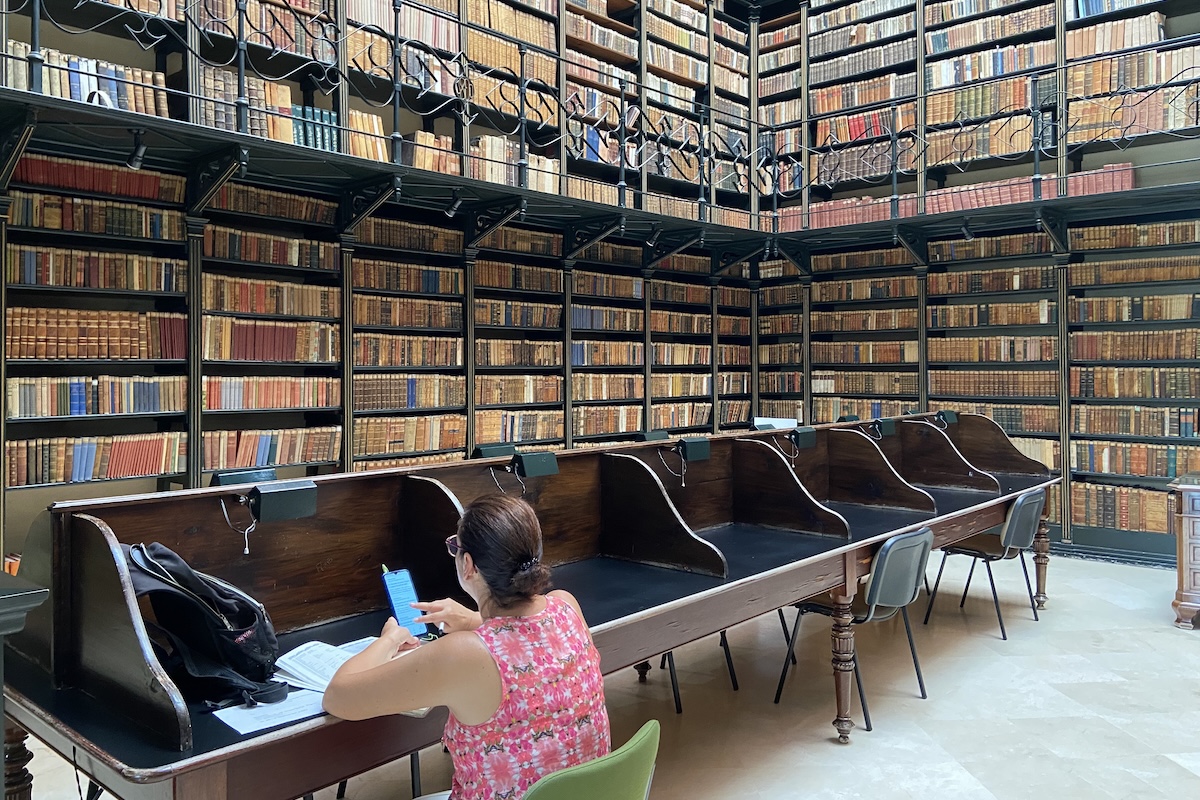 Una donna usa lo smartphone seduta da sola in una sala della biblioteca 