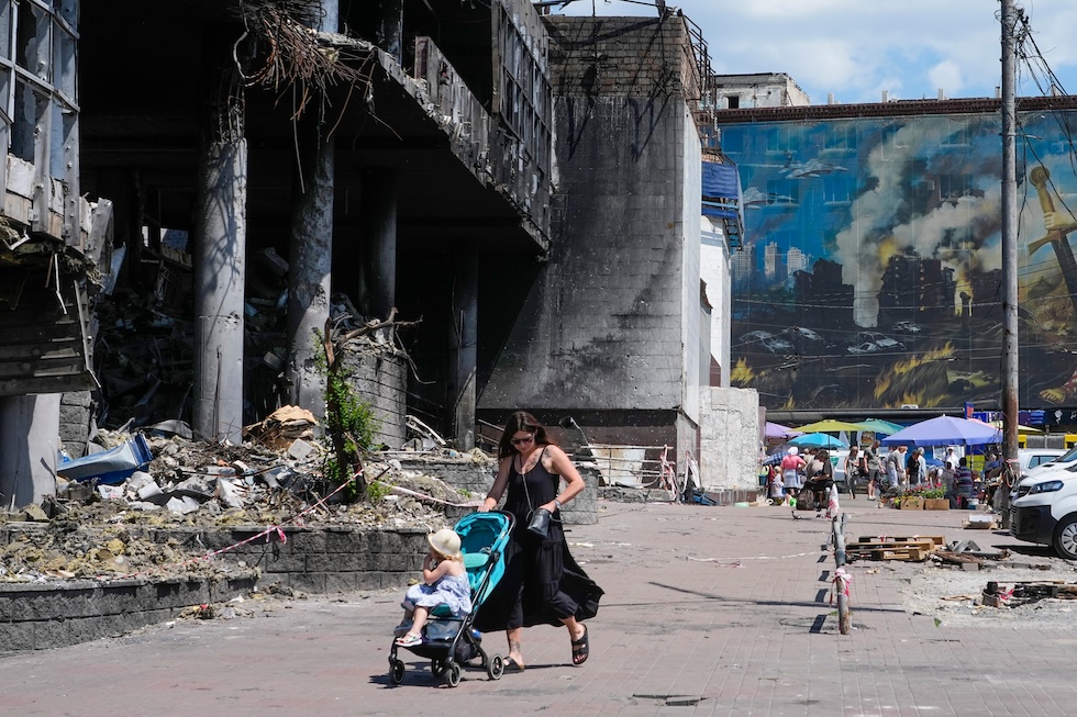 Una donna spinge un passeggino vicino agli edifici danneggiati dagli attacchi russi (AP Photo/Efrem Lukatsky)