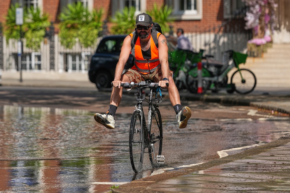 Un uomo in bicicletta alza le gambe per non bagnarsele mentre attraversa una pozzanghera (AP Photo/Kirsty Wigglesworth)