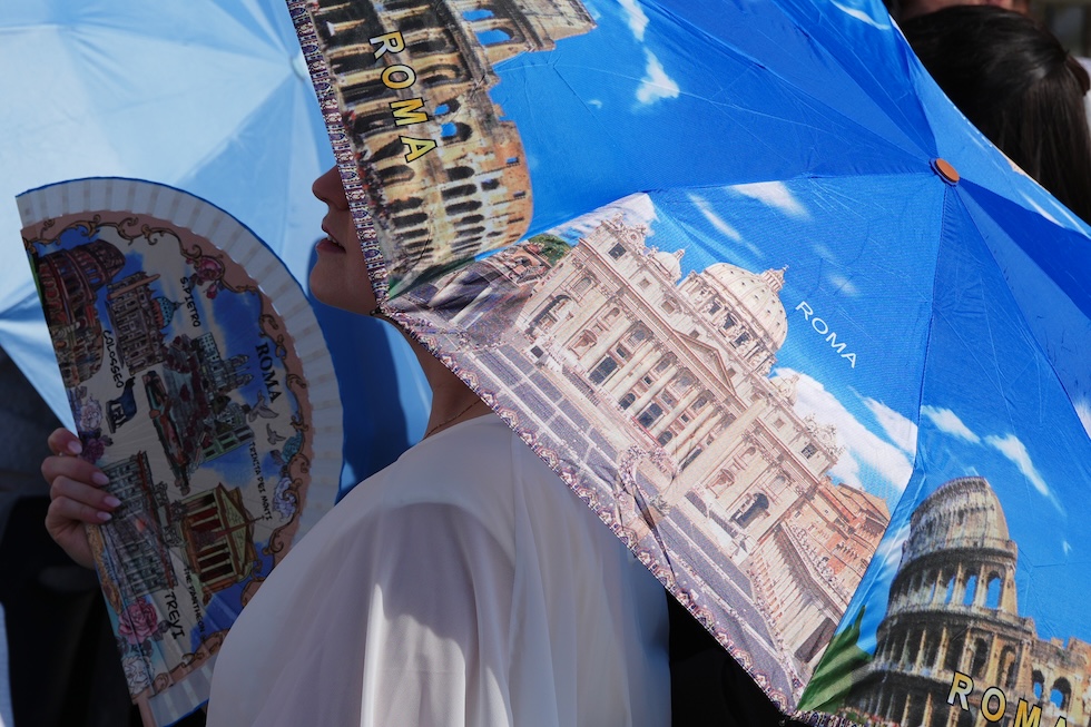 Una fedele cerca di affrontare il caldo con un ventaglio e un ombrello, entrambi a tema Roma, in attesa dell'udienza settimanale di papa Leone XIV (AP Photo/Alessandra Tarantino)
