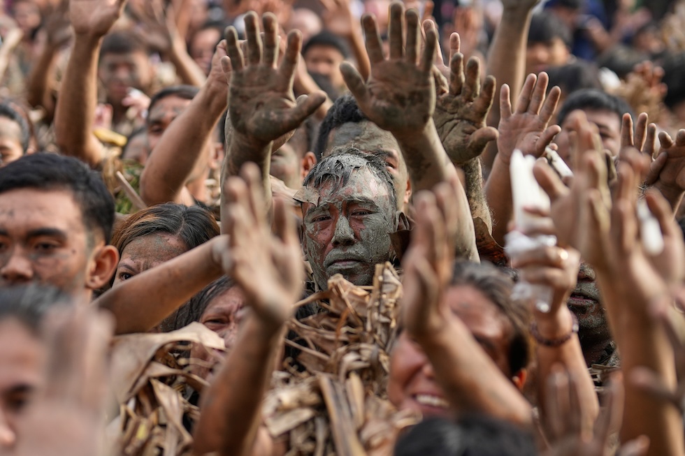 Fedeli cattolici coperti di fango e foglie alzano le mani al cielo durante una messa per il Taong Putik Festival, una celebrazione in onore di san Giovanni Battista (AP Photo/Aaron Favila)

