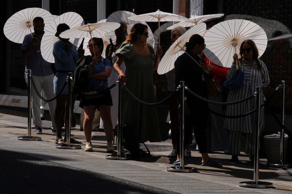 Persone in fila fuori da un negozio si riparano dal sole con degli ombrelli (AP Photo/Kirsty Wigglesworth)
