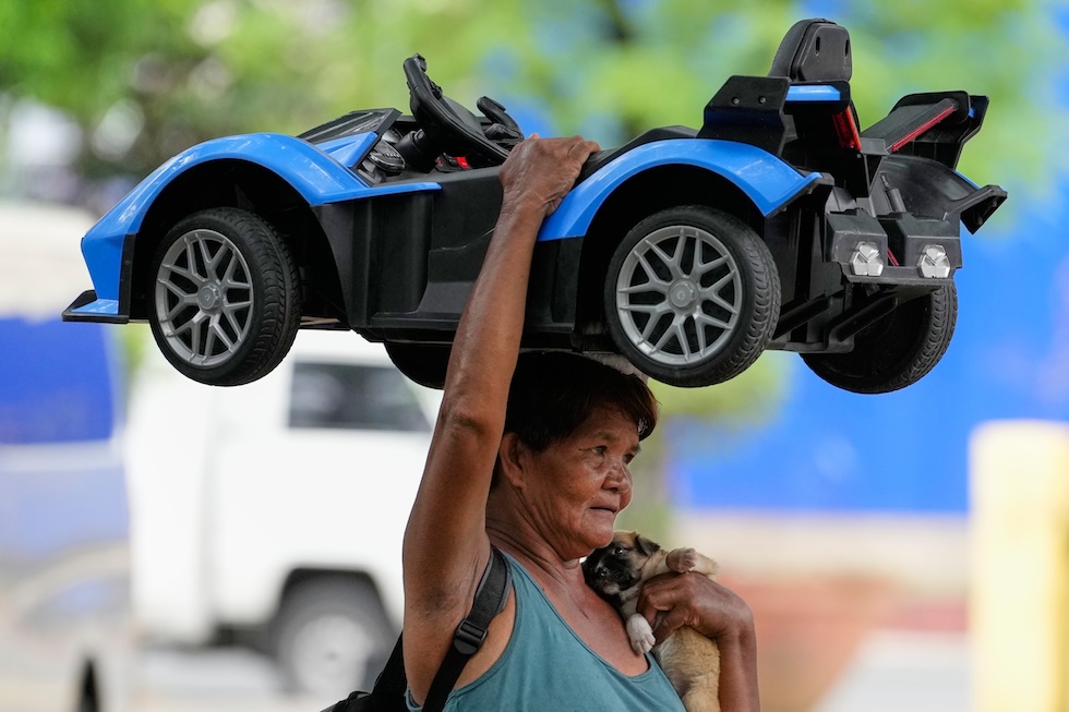 Una donna trasporta un'auto giocattolo mentre tiene in braccio il suo cane (AP/Aaron Favila)
