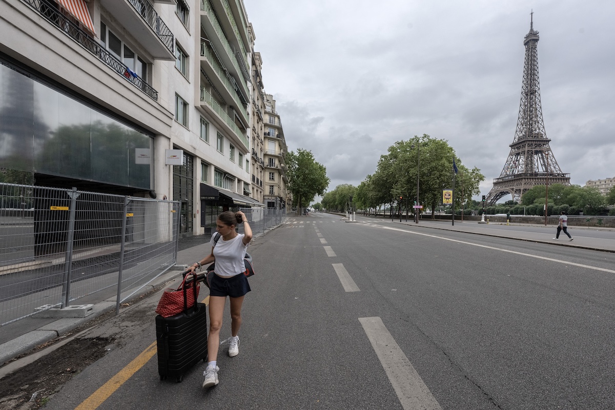 Una ragazza trasporta un trolley e una borsa su una strada, con la Torre Eiffel sullo sfondo