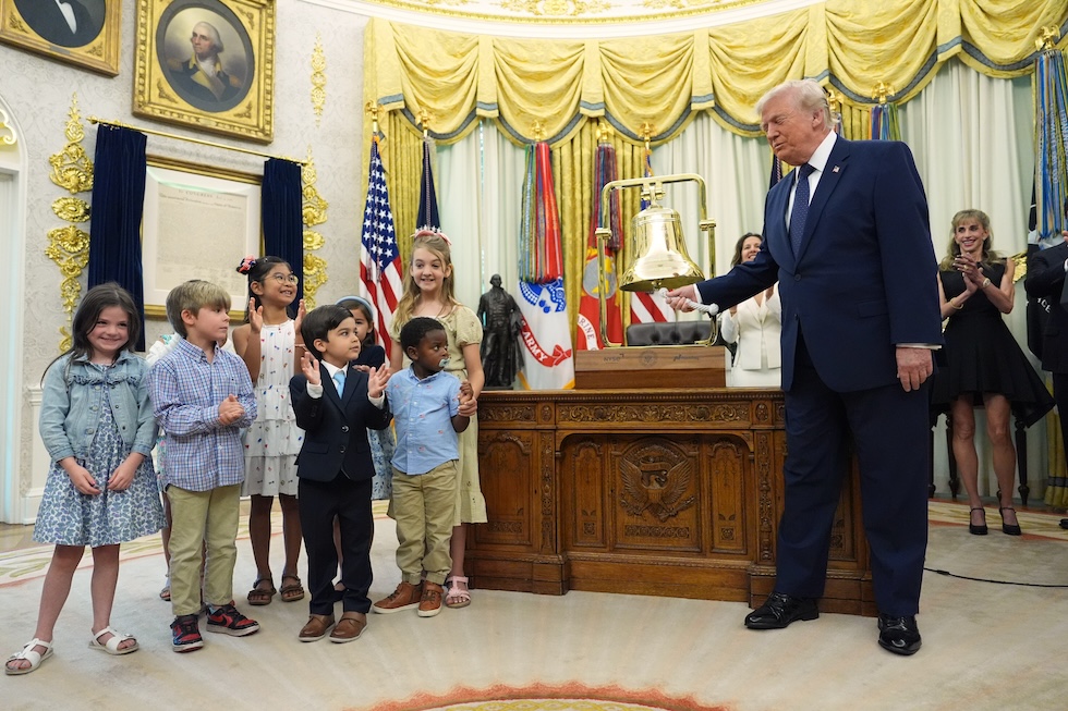 Il presidente degli Stati Uniti Donald Trump suona la campana per l'apertura della Borsa di New York e del Nasdaq nello Studio Ovale della Casa Bianca, davanti a un gruppo di bambini e bambine. L'ha fatto per promuovere i cosiddetti Trump Accounts, che consentono ai minori di avere investimenti legati a indici azionari (AP Photo/Mark Schiefelbein)