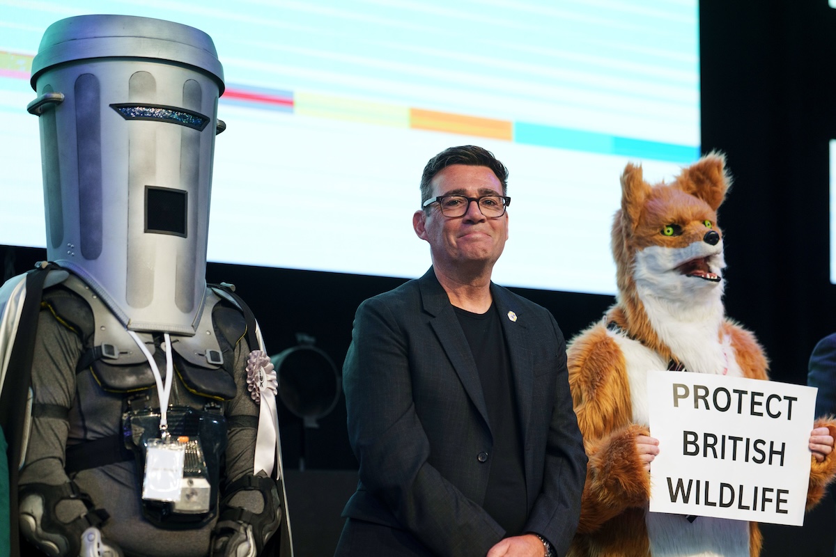 Count Binface (a sinistra) insieme ad Andy Burnham e al candidato del gruppo animalista Protect British Wildlife durante l'annuncio dei risultati delle elezioni suppletive di Makerfield, il 19 giugno 2026.(AP/Jon Super)