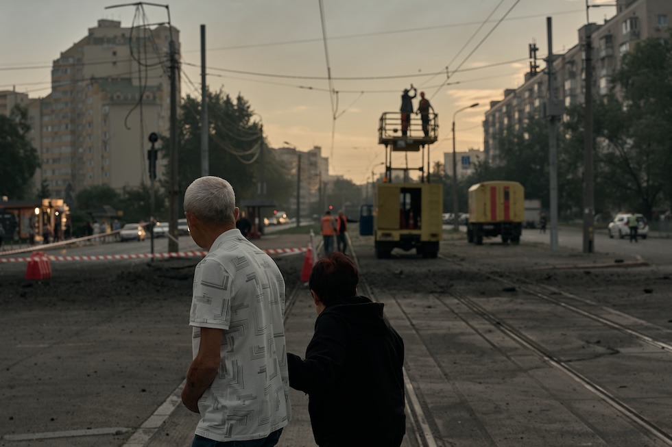 Due persone guardano i lavoratori che riparano le linee dei trasporti pubblici, dopo un attacco russo. (Kostiantyn Liberov/Libkos/Getty Images)
