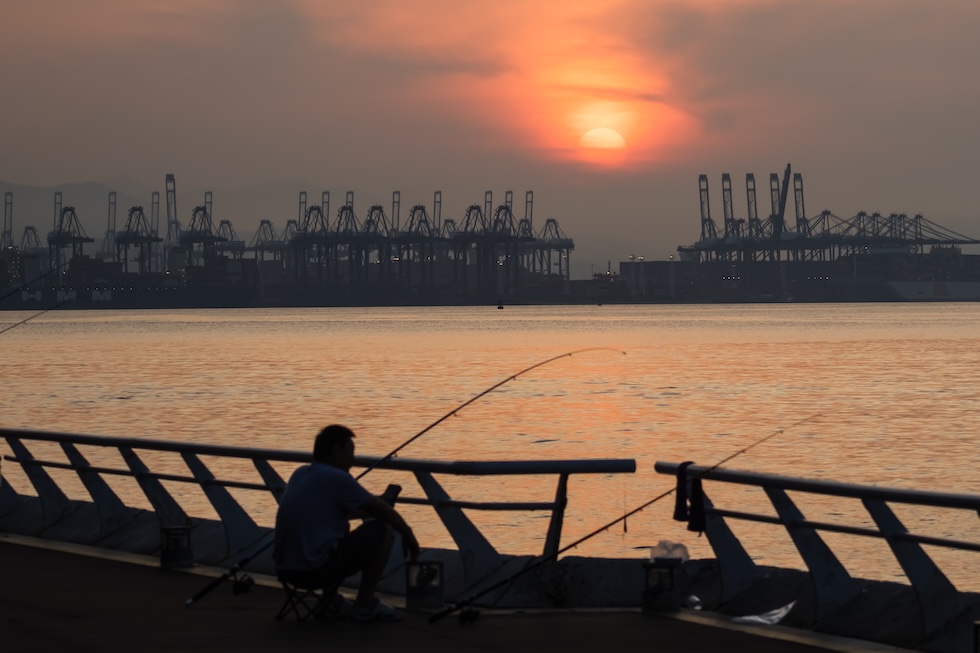 Un pescatore all'alba e sullo sfondo il porto di Yantian (Cheng Xin/Getty Images).